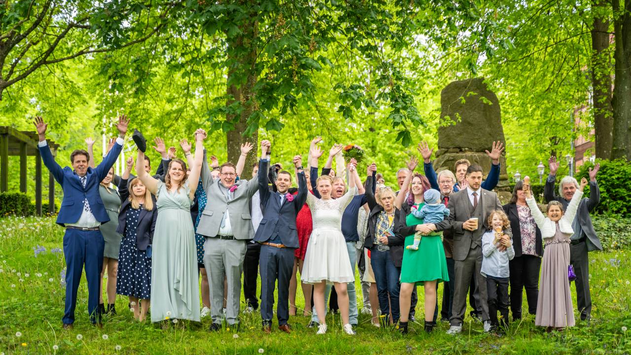 Die Hochzeitsgesellschaft hält freudig ihre Hände in die Luft.